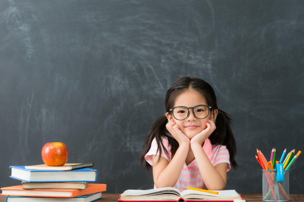 Child sitting with school books and chalkboard 